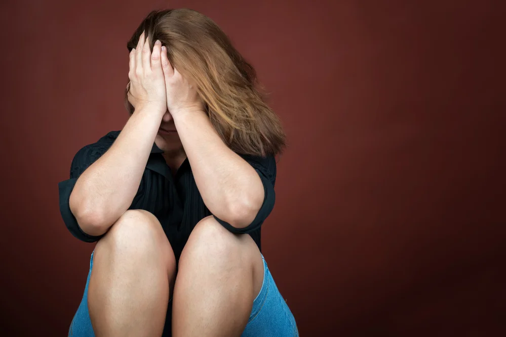 Mujer sentada en el suelo se tapa la cara con manos llorando. Agrsión violencia domestica